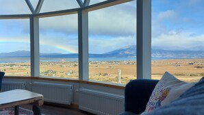 A room with a large window offering a view of a landscape with mountains and a rainbow. - Geodesic Dome with Stunning Glacier and Mountain views (Puerto Natales)