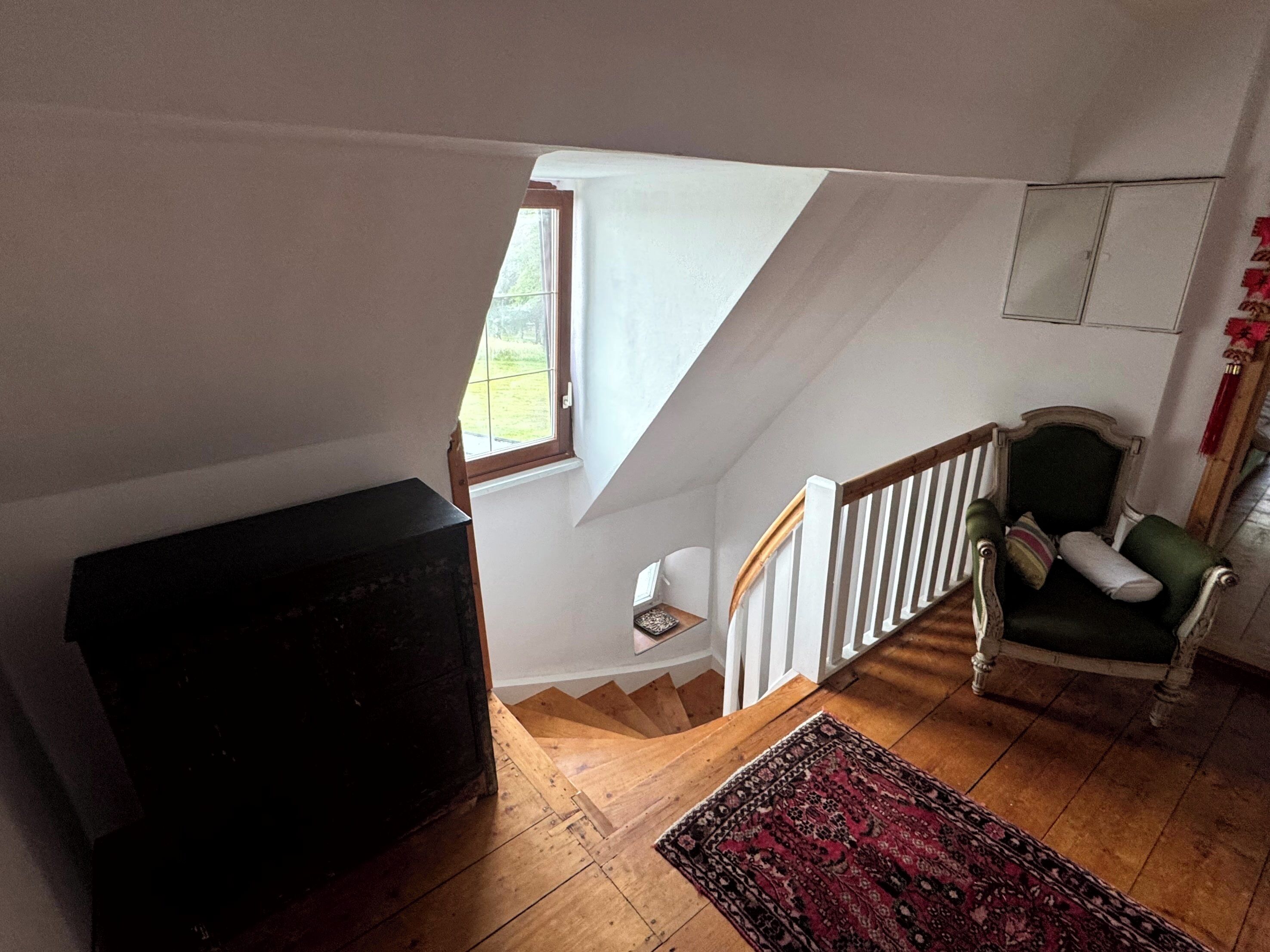 A staircase with wooden steps and white railings, a green armchair with a cushion, and a patterned rug on the floor.