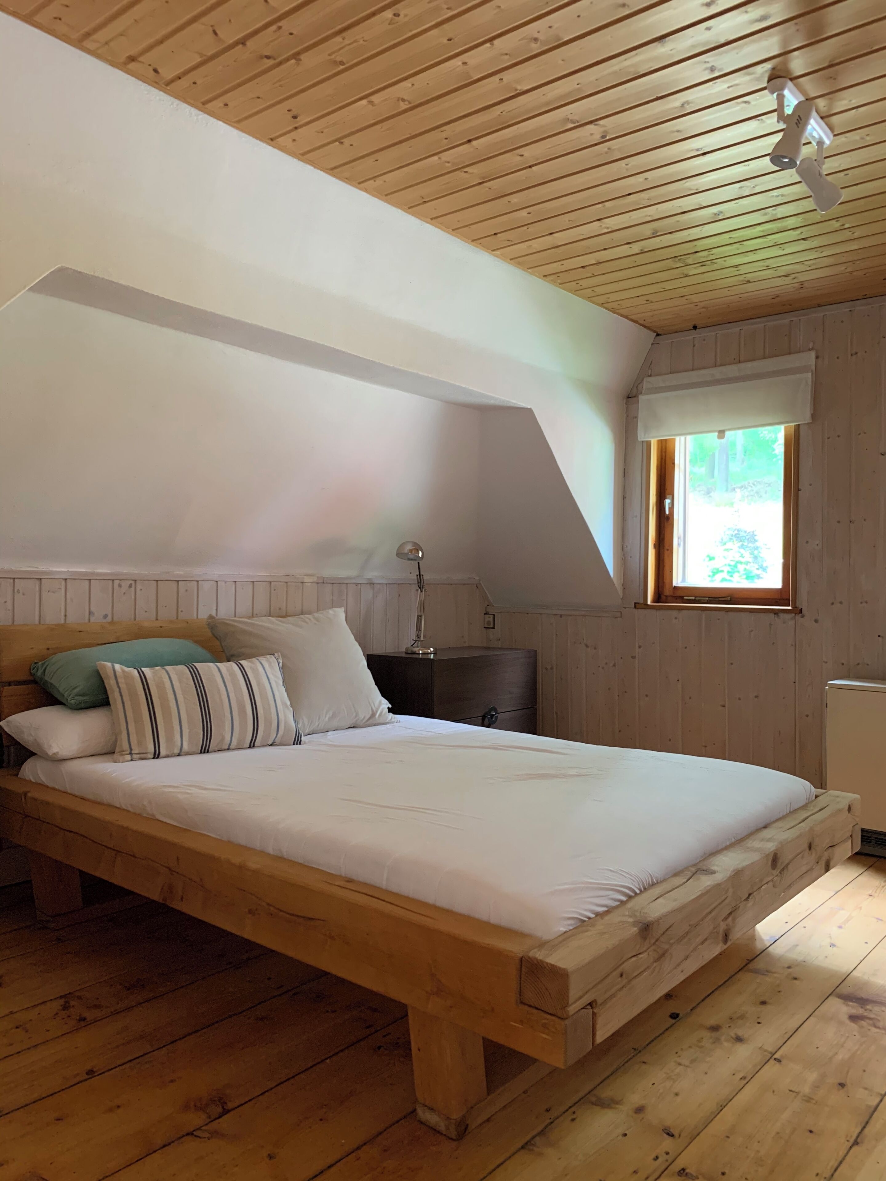 A wooden bed in a room with a sloped ceiling and a window.