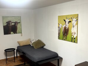 A small bedroom with a bed, two pillows, a bedside table, and two wall-mounted paintings of animals.