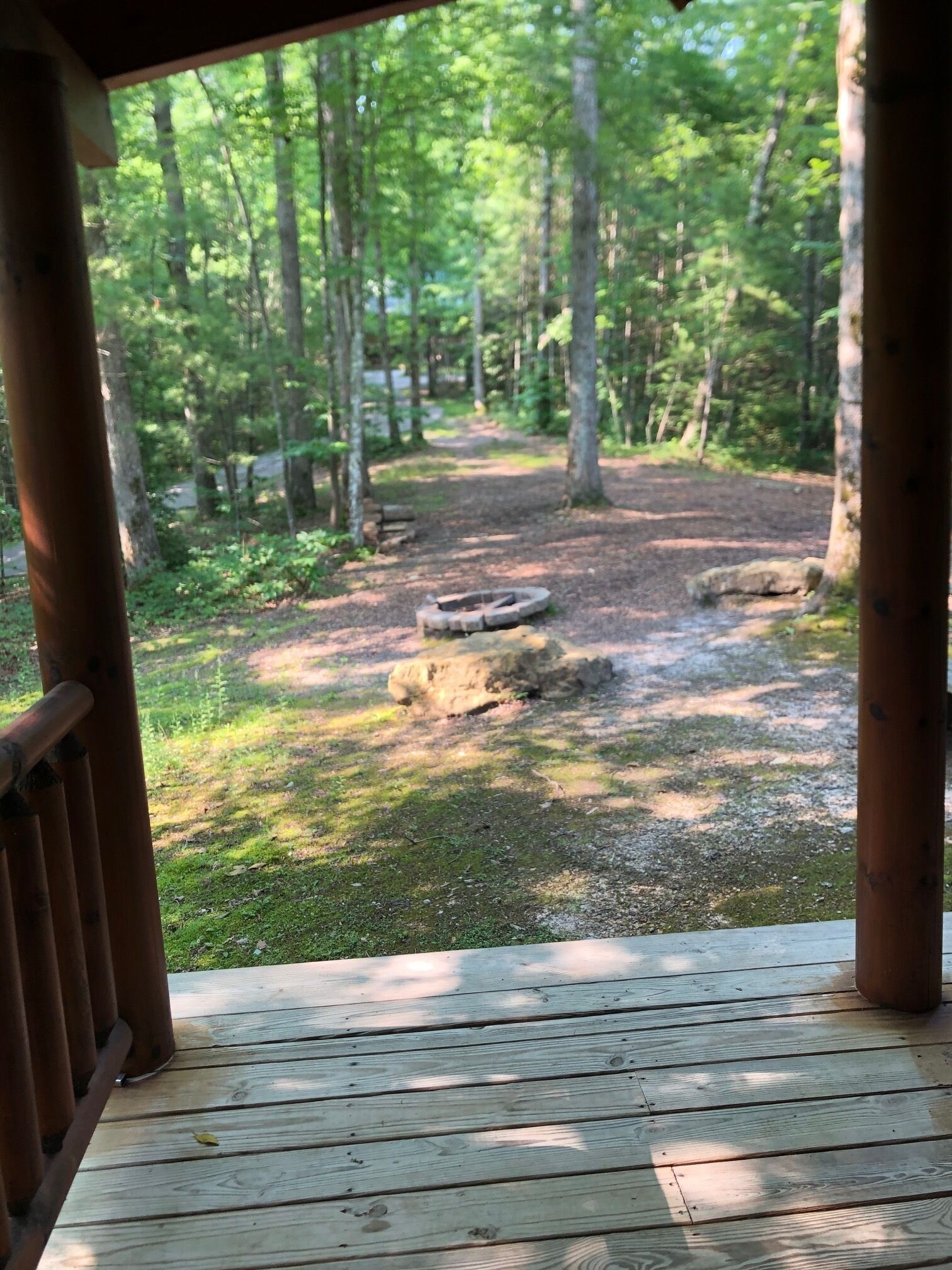 A wooden deck with a view of a forested area and a fire pit.