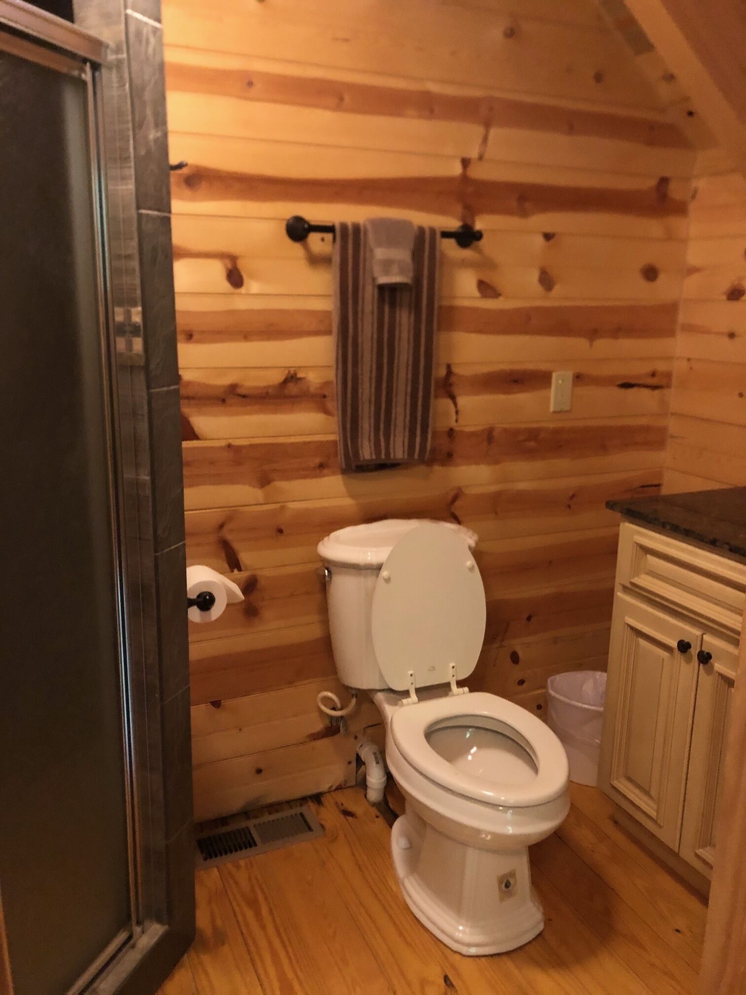 A wooden cabin bathroom with a toilet, a shower area, and a wooden cabinet.