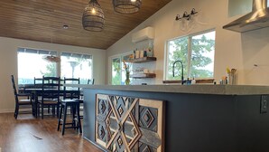 Cocina moderna con isla de madera, comedor y ventanas amplias.