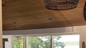 Una sala de estar moderna con un ventanal grande, techo de madera y un florero sobre una mesa.