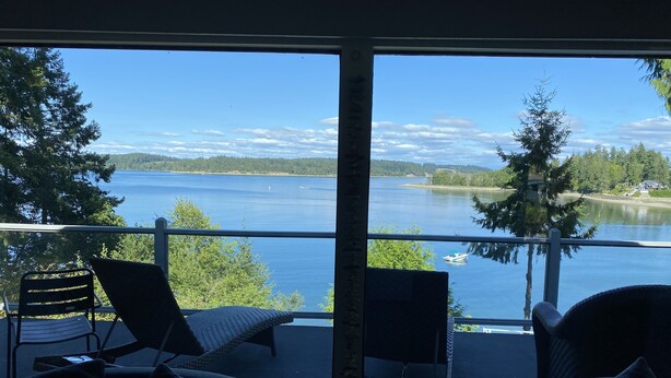 Un balcón con dos sillones y una mesa, con vista a un lago con un bote y árboles.