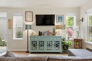 A living room with a television, a cabinet with glass doors, a lamp, and a window with an American flag.