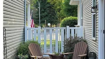 Relax in this serene outdoor space with two Adirondack chairs and a small table, surrounded by a picket fence and string lights.