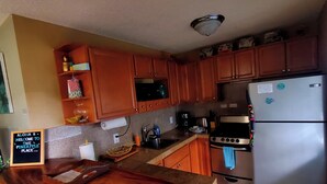 A kitchen with wooden cabinets, a stainless steel refrigerator, a stove, and a countertop with various items.