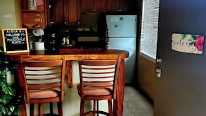 A kitchen with wooden cabinets, a refrigerator, and a bar area with two chairs.