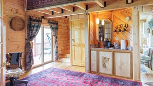 A log cabin interior with a wooden ceiling, a red patterned rug, a wooden bench, a door leading outside, and a kitchen area with a bear and deer carved into the cabinet doors. - The Lodge at Joe Walker Hollow, privacy at its best with plenty of family space (Middlebrook)