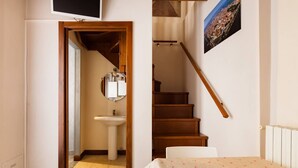 Ein Schlafzimmer mit Bett, einer Holztreppe, einem Badezimmer mit Waschbecken und einem an der Wand montierten Fernseher.