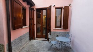 Eine kleine Terrasse mit Tisch und Stühlen, einer Tür und einem Fenster mit Rollläden.