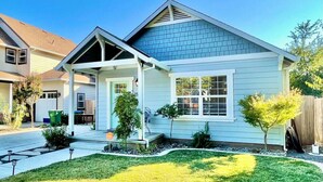 Ein eingeschossiges Haus mit Satteldach, einer Veranda und einem Vorgarten mit kleinen Bäumen und Sträuchern.