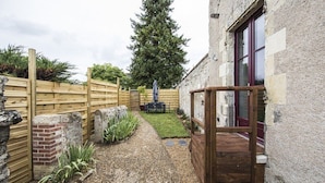 A rustic garden with a wooden fence, a stone wall, and a gravel path leading to a wooden gate.