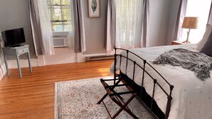 Une chambre à coucher avec un lit, un téléviseur posé sur un meuble, un radiateur et une fenêtre avec des rideaux.