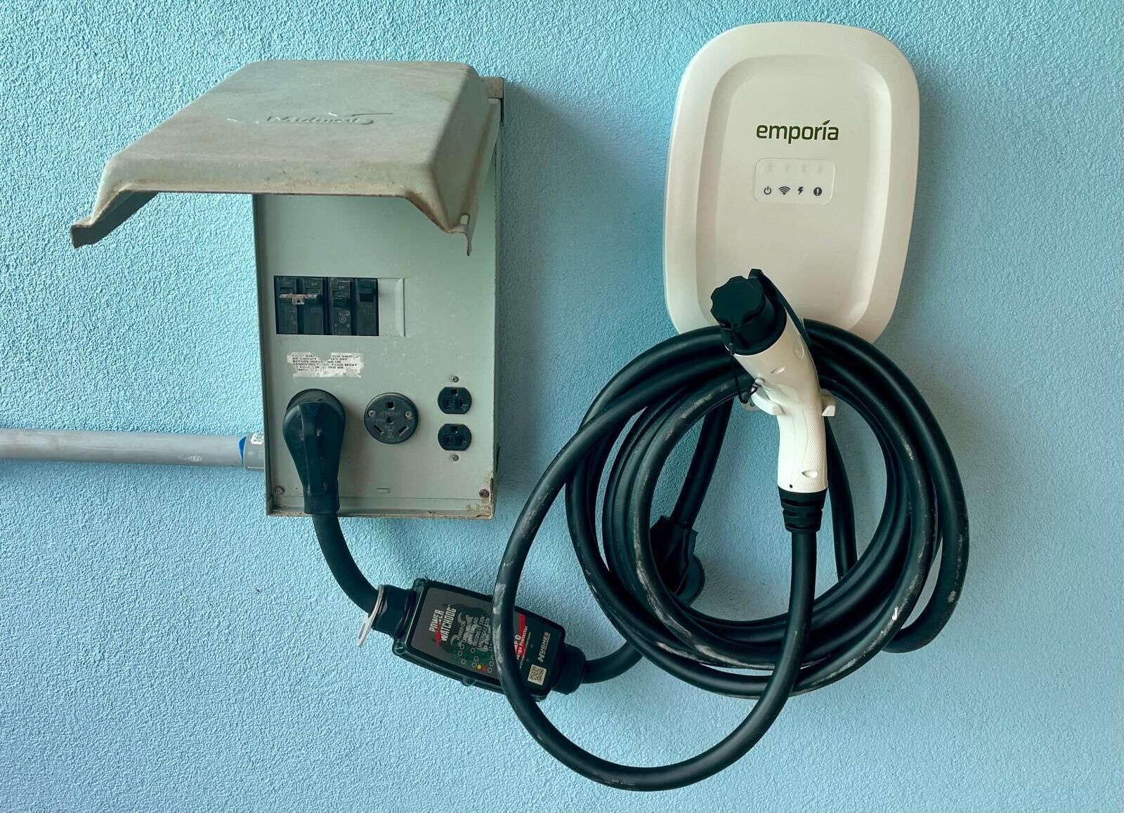 Un enchufe con un tapón conectado a un dispositivo, y una caja eléctrica empotrada en la pared con una etiqueta.