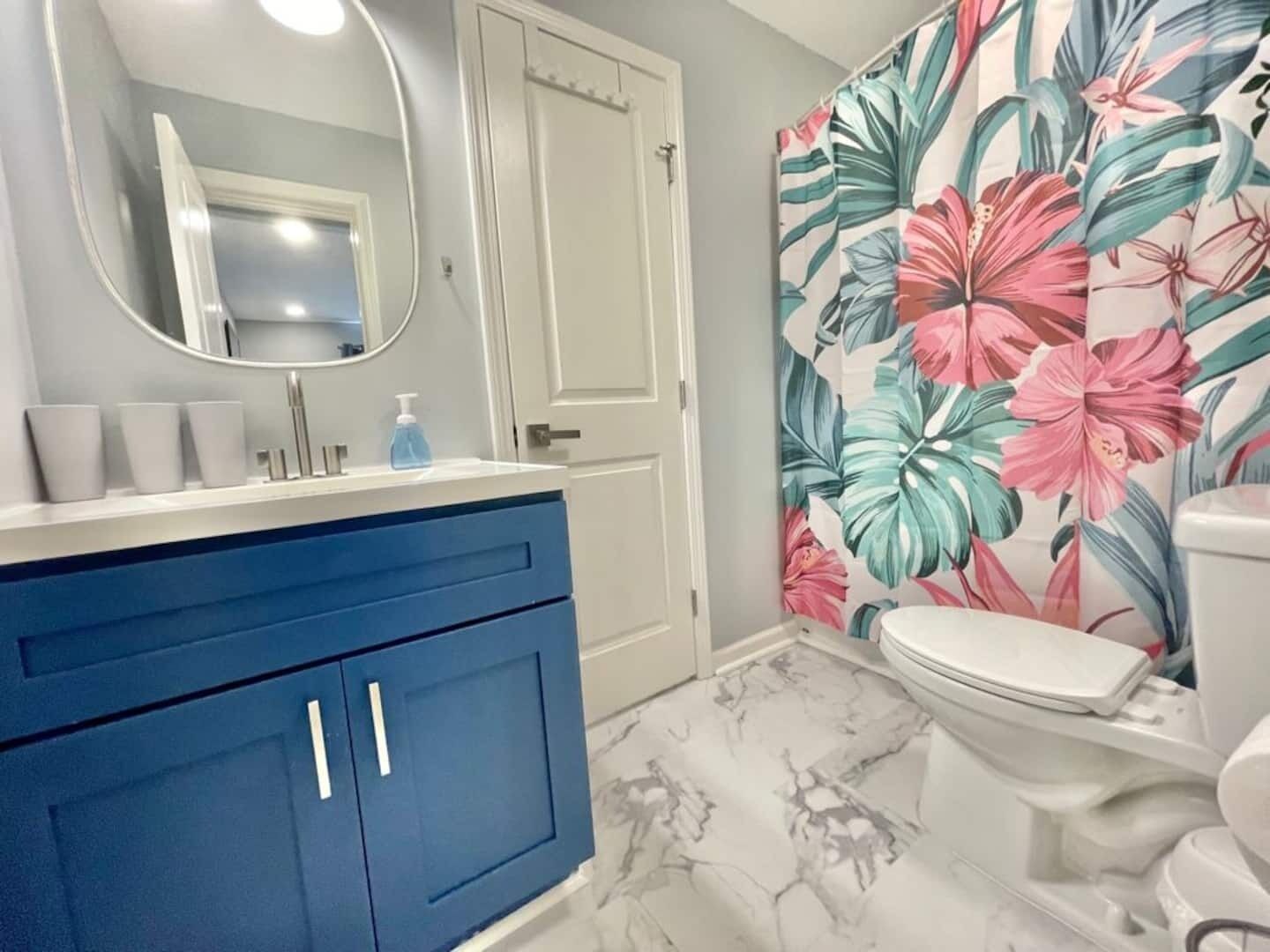Un baño con un tocador azul, un inodoro blanco y una cortina de ducha estampada con motivos florales.