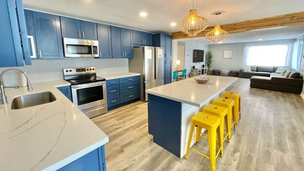 Una cocina moderna con armarios azules, electrodomésticos de acero inoxidable y una isla central con taburetes amarillos.