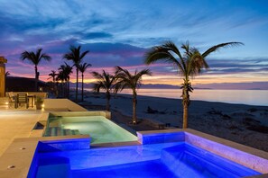 A pool area with a sunset view, palm trees, and a beach in the background.
