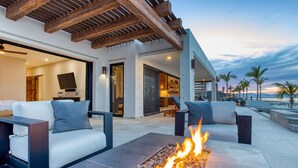 Una zona exterior moderna amb un element decoratiu de foc, seients confortables i vistes a la platja al capvespre.