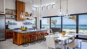 Cuina moderna amb una illa central, tamborets de bar i zona de menjador amb vista a l'oceà.