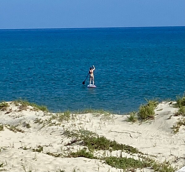 A person paddleboarding on a calm sea with a sandy beach in the foreground.
