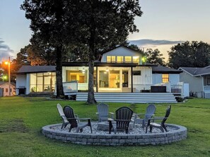 Een modern huis met een groot terras, een vuurplaats met stoelen en een verzorgd gazon.