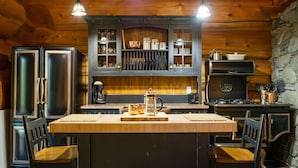 A rustic kitchen with wooden cabinets, a central island, and a stone wall. - Copper Cabin- Hot Tub, Luxury, Romantic (Ucluelet)