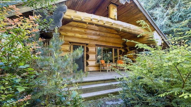 A log cabin with a porch, wooden steps, and a dining area with chairs. - Copper Cabin- Hot Tub, Luxury, Romantic (Ucluelet)