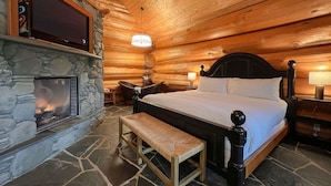A log cabin bedroom with a stone fireplace, a bed with white linens, a wooden bench, and a stone floor. - Copper Cabin- Hot Tub, Luxury, Romantic (Ucluelet)