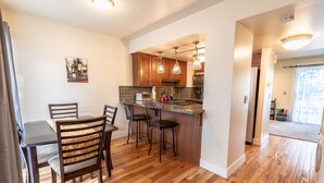 A modern kitchen with wooden cabinets, a bar area, and a dining table with chairs.