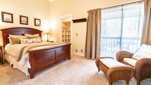 A bedroom with a wooden bed, a nightstand, a chair, a closet, and a large window with curtains.