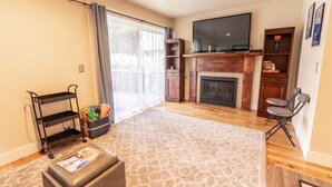 A living room with a fireplace, a TV mounted above it, a sofa, a coffee table, and a bookshelf.