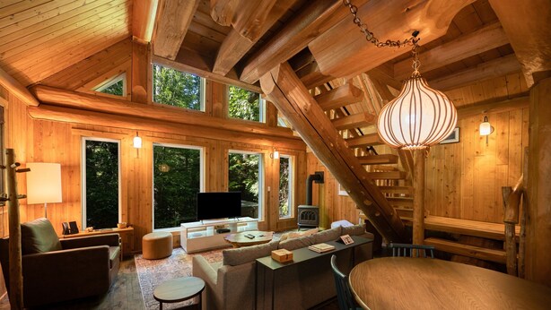 A cozy log cabin interior with a fireplace, comfortable seating, and large windows offering a view of the forest. - Halfmoon Cottage I Nature Escape I Hot Tub I Pets (Ucluelet)