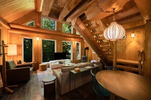 Een gezellig houten blokhutinterieur met een open haard, comfortabele zithoek en grote ramen met uitzicht op het bos.