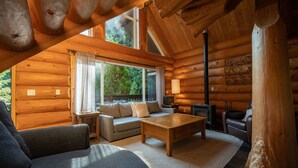 A cozy log cabin interior with a sofa, a coffee table, and a fireplace. - Willowbrae Chalet-Sophisticated Forest-Hot Tub (Ucluelet)