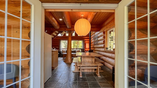 A log cabin interior with a central wooden table and benches, a hanging lantern, and a view of the surrounding forest. - Willowbrae Chalet-Sophisticated Forest-Hot Tub (Ucluelet)