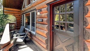 A log cabin with a wooden exterior, a front door with glass panels, and a porch with outdoor seating. - Willowbrae Chalet-Sophisticated Forest-Hot Tub (Ucluelet)