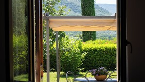 Een raam met uitzicht op een tuin, een houten pergola en een tafel met een bloemenmand.
