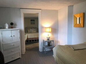 A bedroom with a bed, a nightstand with a lamp, a dresser, and a door leading to another room. - Steps to the beach (Seaside Park)