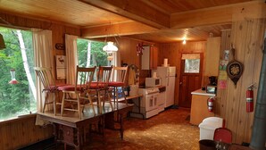 A cozy cabin interior with a wooden dining table, chairs, a small kitchen area with a stove and refrigerator, and a fireplace. - Cottage with 40' Dock!  Beautiful lake with excellent fishing. (Port loring)