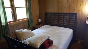 A wooden-paneled room with a bed, a nightstand, a lamp, and a window with curtains. - Cottage with 40' Dock!  Beautiful lake with excellent fishing. (Port loring)