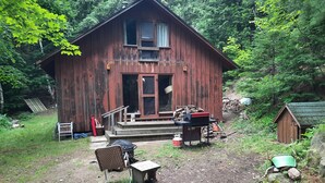 A rustic wooden cabin with a porch, surrounded by dense forest. - Cottage with 40' Dock!  Beautiful lake with excellent fishing. (Port loring)