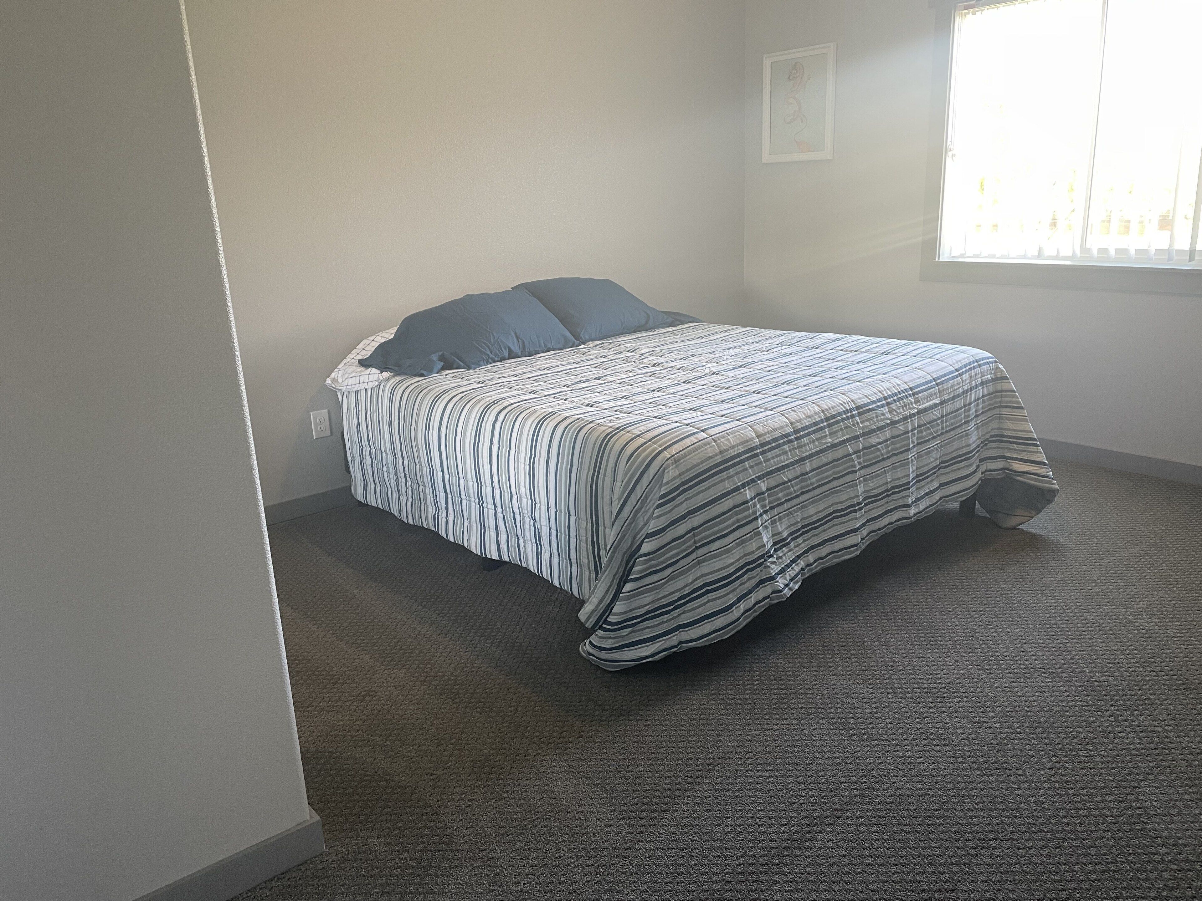 Un dormitorio con una cama, una ventana y piso cubierto de alfombra.