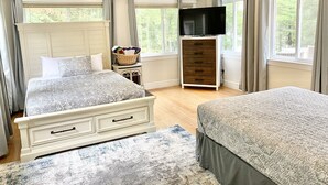 A bedroom with two beds, a TV on a dresser, and large windows with curtains. - LAKE HOME! HOT TUB, GYM, FREEgolf cart, 2 kitchens (East Waterboro Maine)