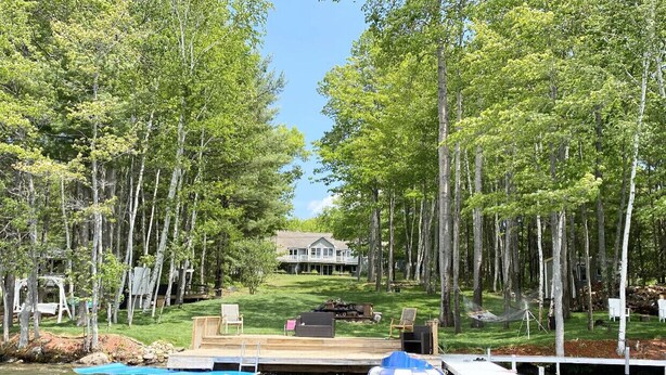 A lakeside property with a dock, a house in the background, and a grassy area with outdoor furniture. - LAKE HOME! HOT TUB, GYM, FREEgolf cart, 2 kitchens (East Waterboro Maine)