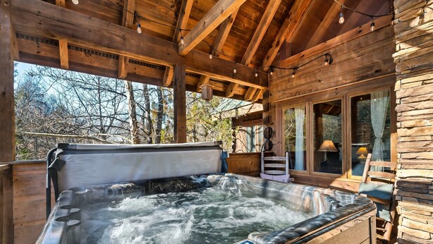 A wooden cabin with a hot tub, stone walls, and large windows.