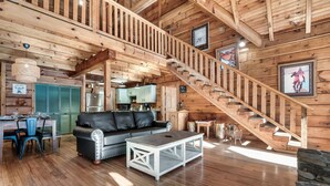 A spacious wooden interior with a staircase, a dining area, and a living room with a sofa and coffee table.