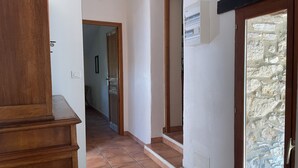 Een gang met een houten kast, betegelde vloer, stenen muur en een deur met glas-in-lood.