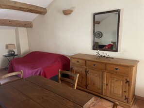 Ein Zimmer mit einem Holzesstisch, einem Bett mit roter Auflage, einem Holzschrank und einem an der Wand befestigten Spiegel.